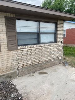 A brick building with a window, shutter, and concrete patio, viewed from the outside on an overcast day.