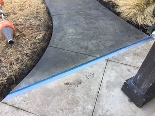 Gray stamped concrete pathway with blue tape next to a concrete slab.