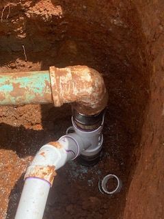 Pipes connected in an underground hole. Rusty metal elbow connects to white and black PVC pipes.