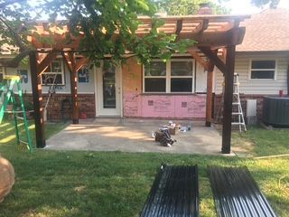 Pergola built over a patio; home in the background; construction materials in yard.