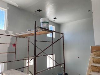Interior wall painting in progress with scaffolding, paint bucket, and windows.