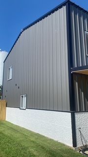 Gray metal-sided building with a white stucco base, small windows, and green lawn. Blue sky background.