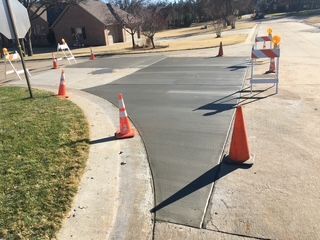 Freshly poured concrete road repair; orange cones and barricades block access; sunny day.