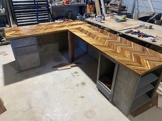L-shaped desk with herringbone pattern wood top on concrete block base in a workshop.