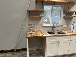 A kitchen remodel in progress; white cabinets, wood shelves, a sink, and a herringbone backsplash.