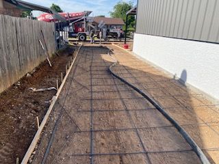 Concrete being poured for a walkway. Steel rebar grid laid. Concrete truck, fence and house visible.