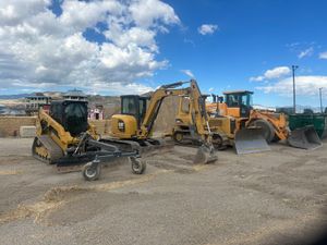 A group of construction vehicles are parked in a dirt lot.