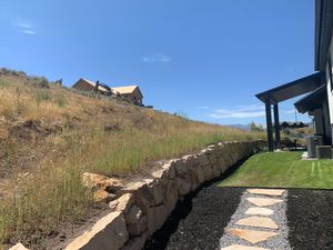 A stone wall surrounds a lush green yard with a house in the background.