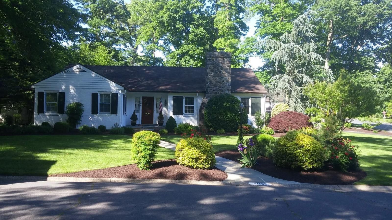 A white house with black shutters is surrounded by trees and bushes.