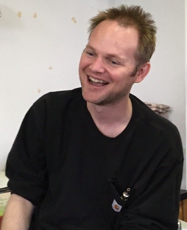 A man in a yellow vest is adjusting a thermostat while holding a tablet.