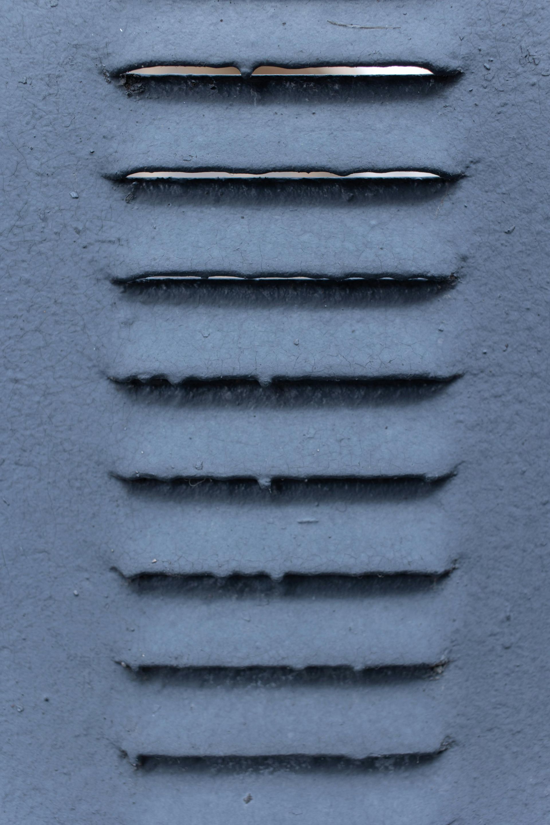 A series of eight horizontal ventilation slits on a textured, blue-gray metal surface.