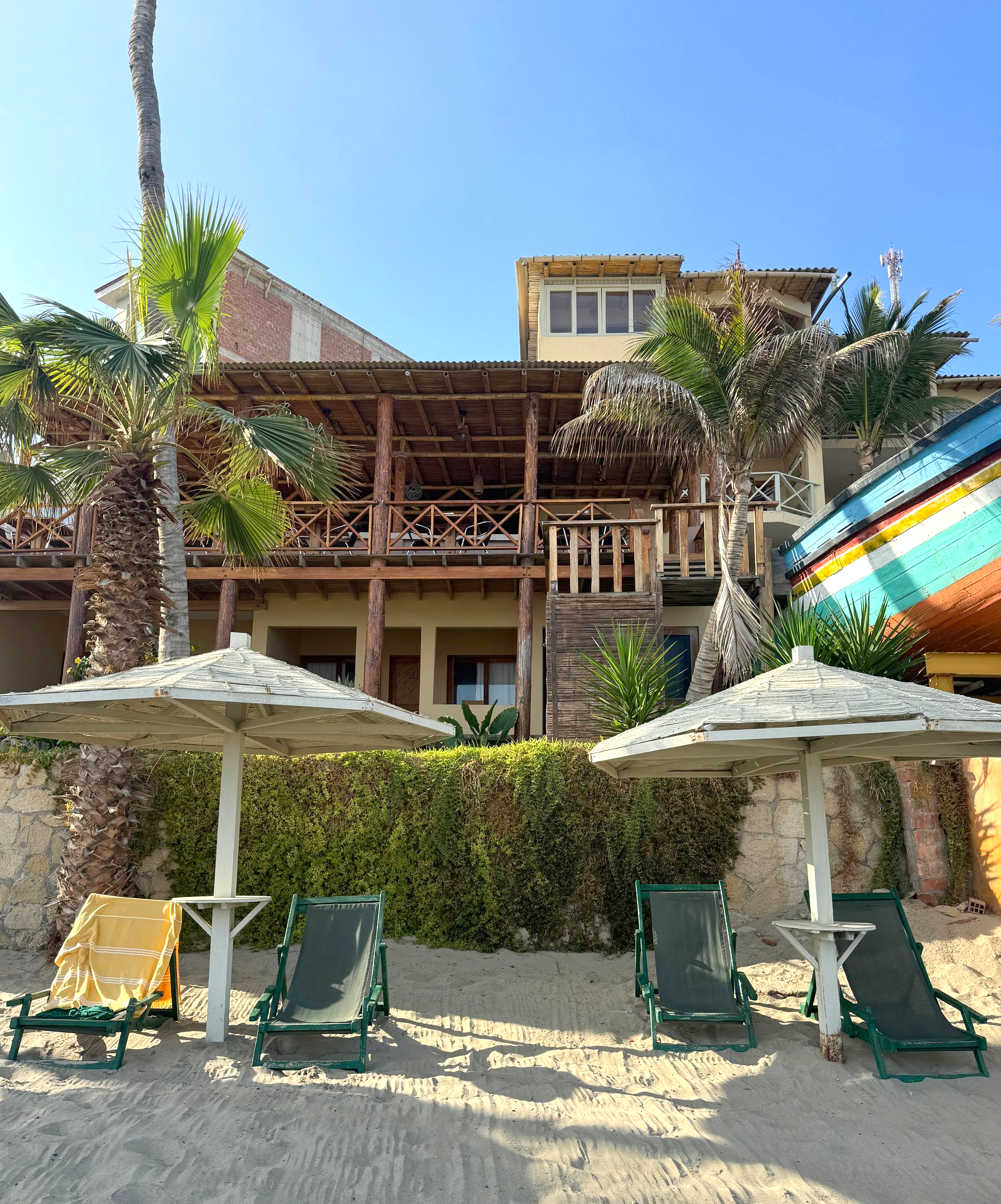 Beachfront resort with lounge chairs and umbrellas; building with wooden balconies.