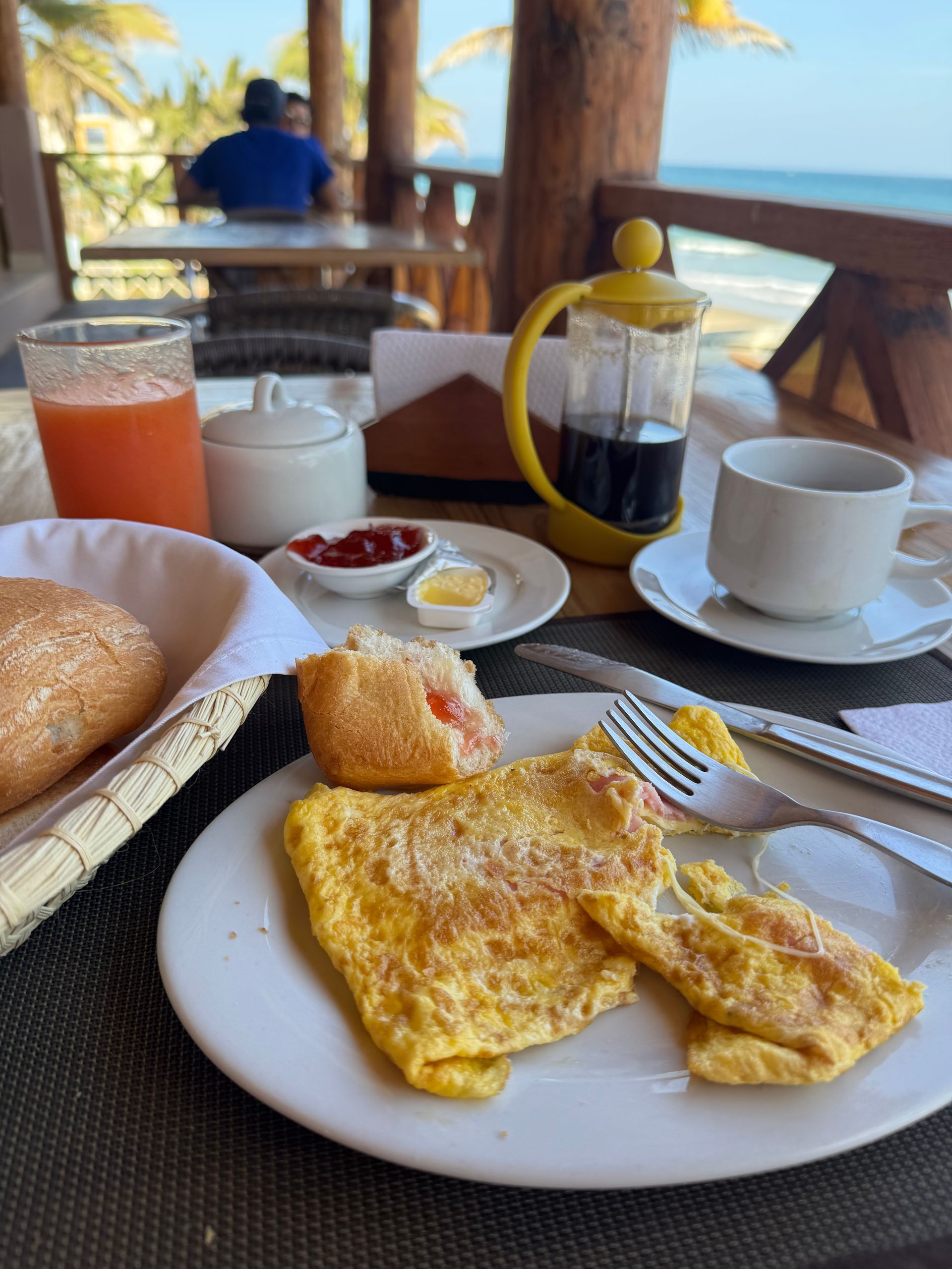 Breakfast on a beachfront patio: omelet, bread, juice, coffee, and ocean view.