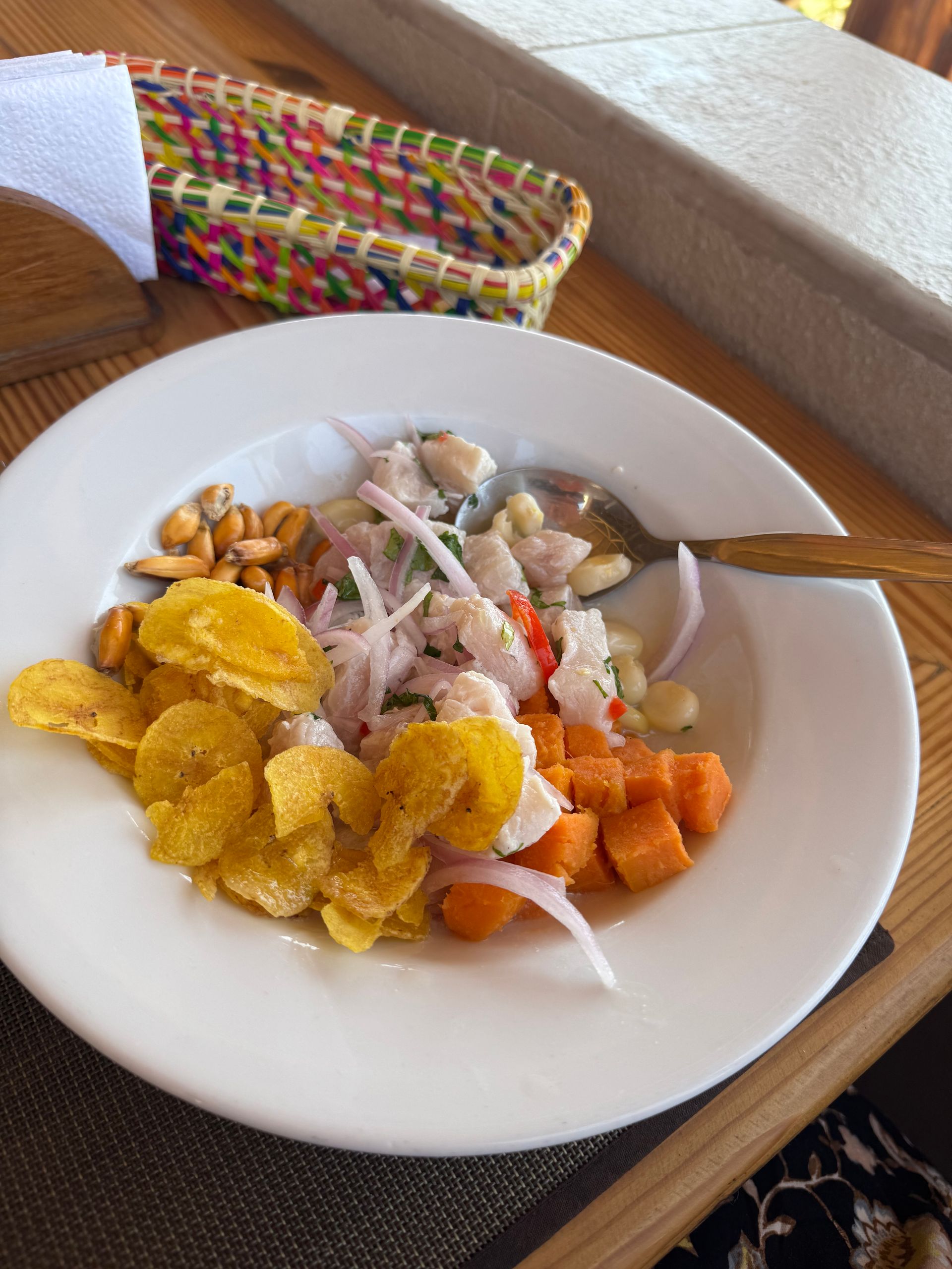 Ceviche dish with plantain chips, sweet potato, onions, and corn in a white bowl.