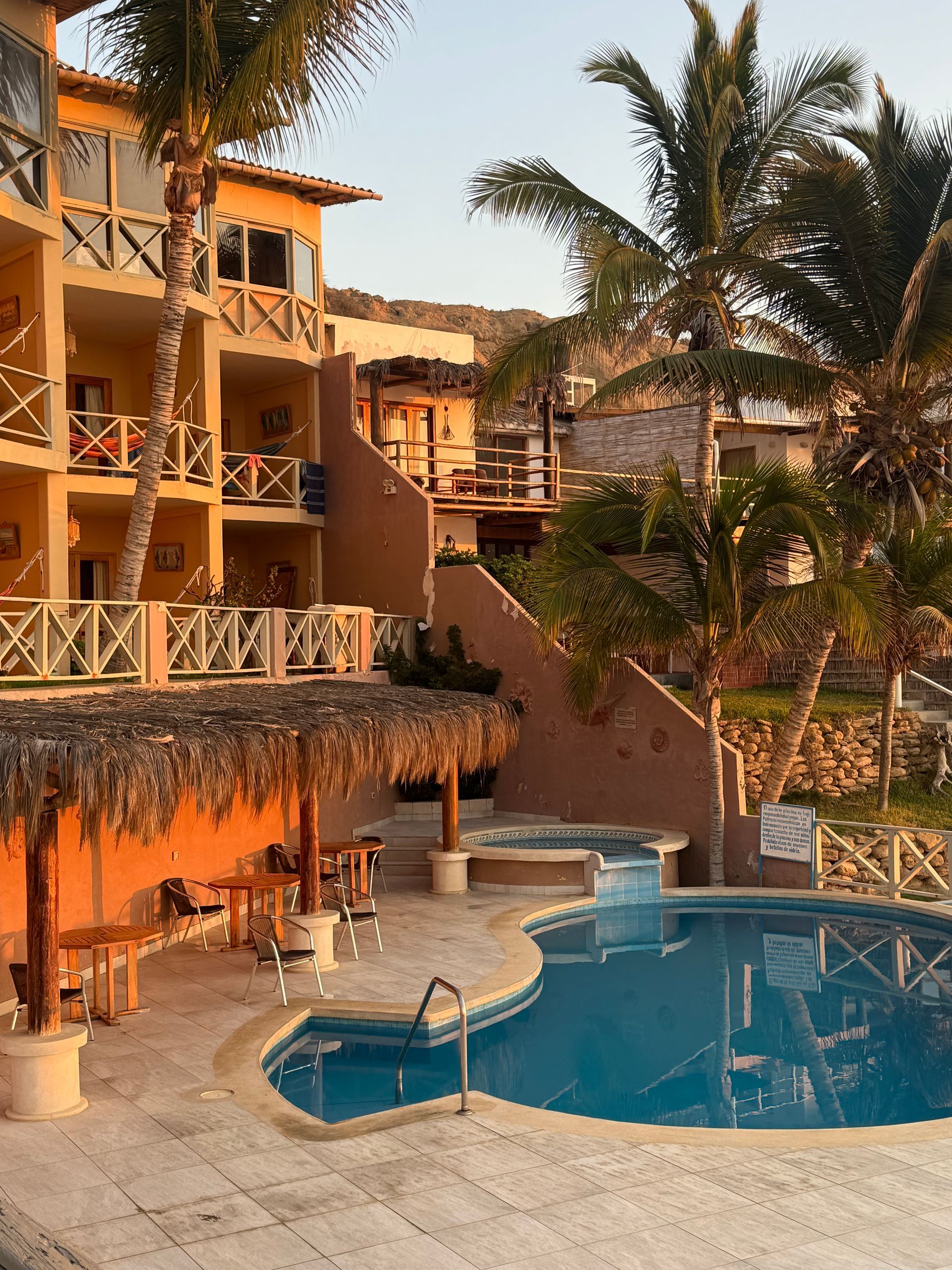 Resort with pool, palm trees, and buildings in warm sunlight.