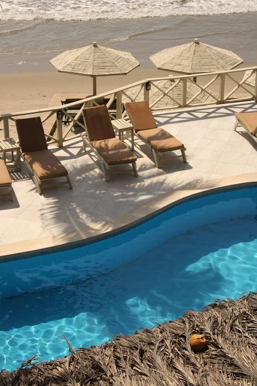 A large swimming pool surrounded by chairs and umbrellas on a beach.