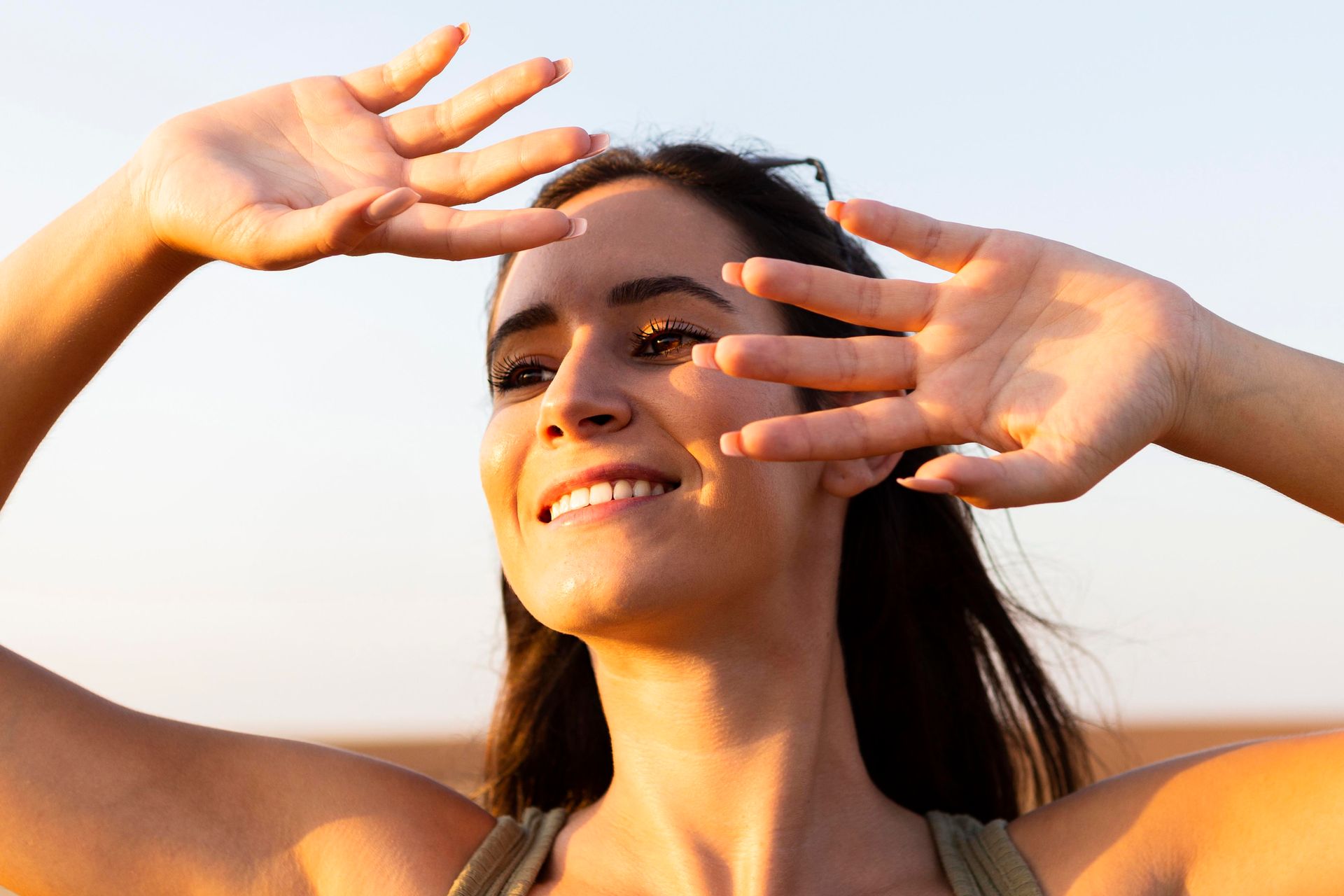 A woman is covering her eyes from the sun with her hands.