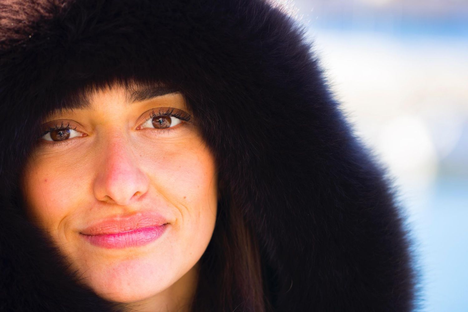 Woman with brown eyes smiles, wearing a black fur-trimmed hood.
