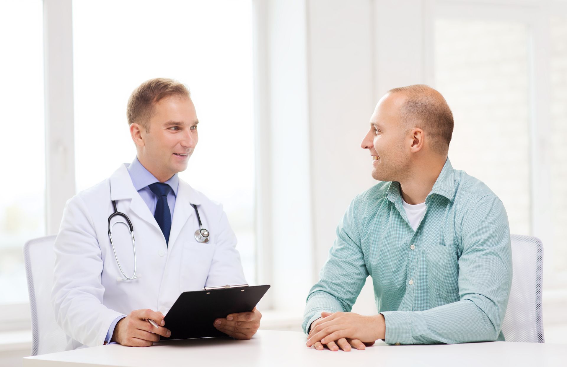 Doctor in white coat with stethoscope reviews chart with patient in office setting.