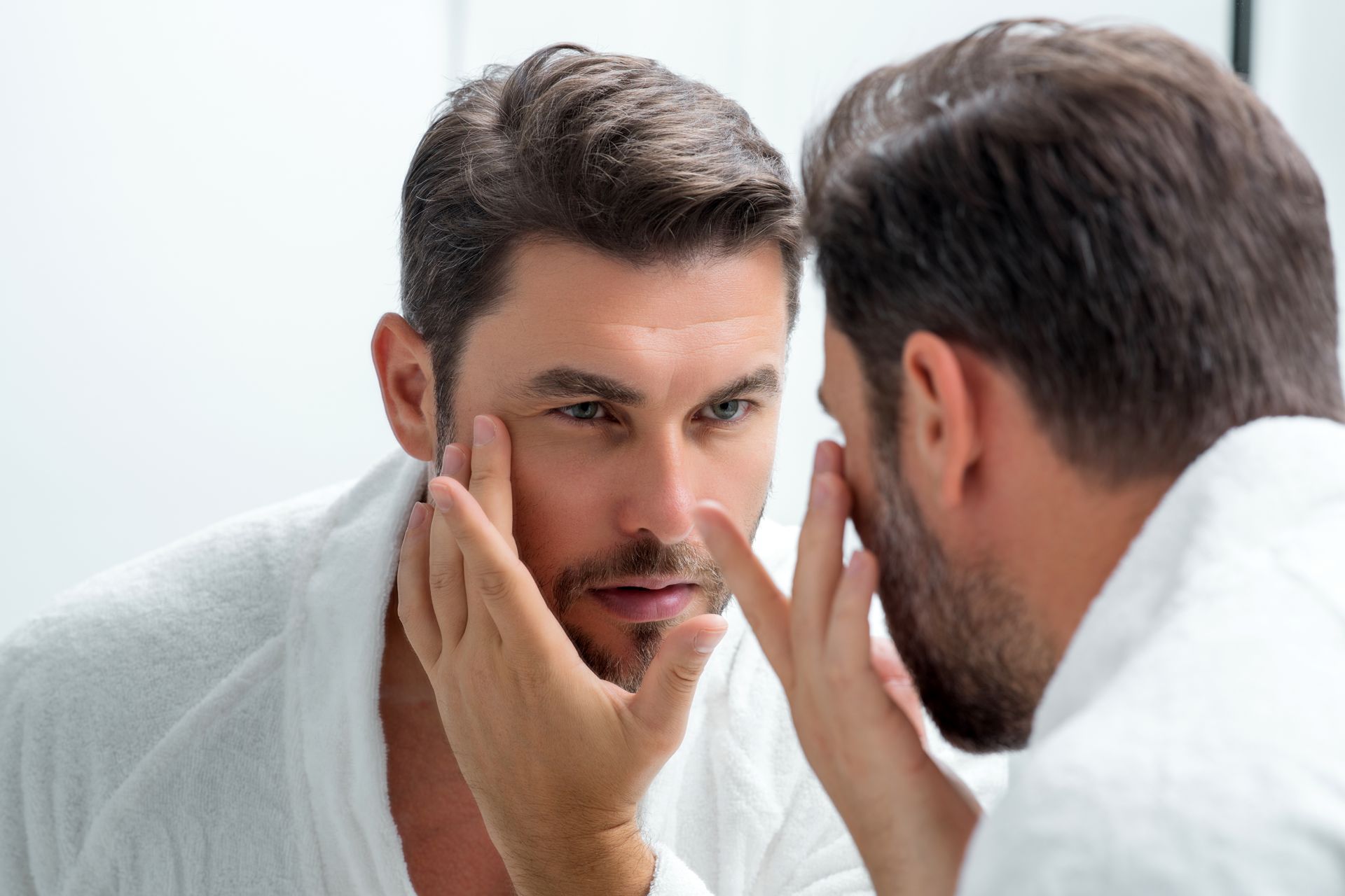 A man is looking at his face in the mirror.