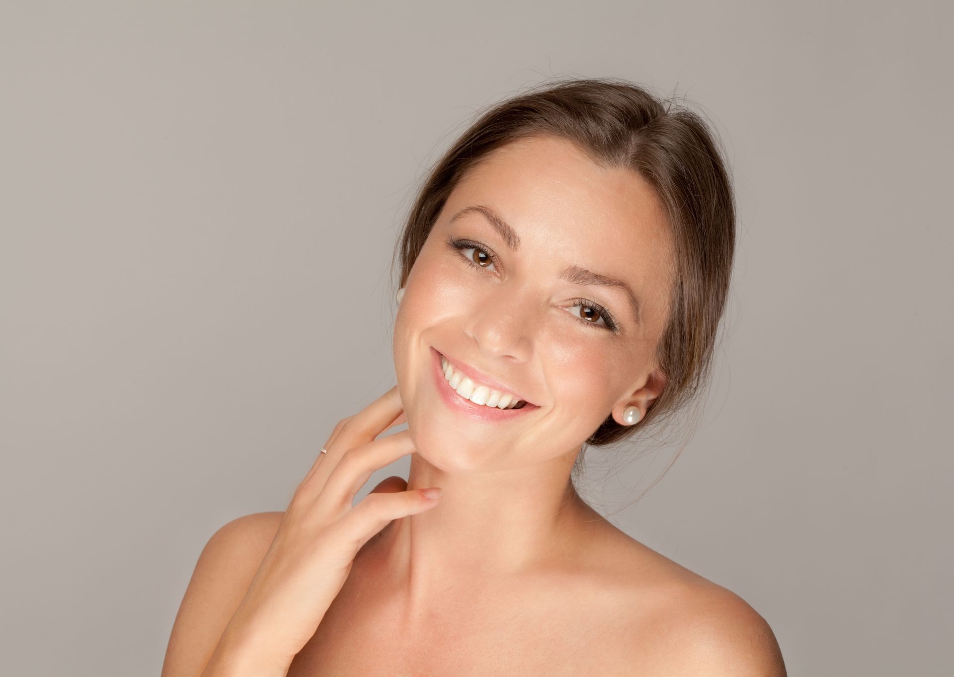 A woman is smiling and touching her face with her hand.