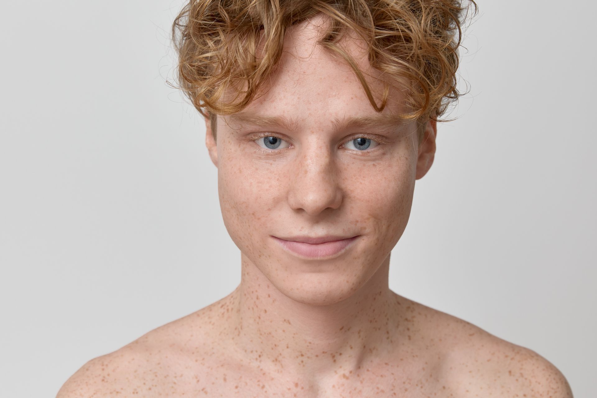 A shirtless young man with red hair and freckles is smiling at the camera.