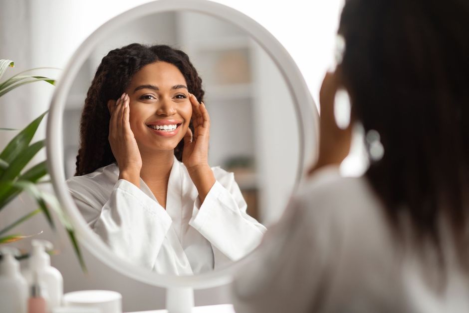 A woman is smiling while looking at her face in a mirror.