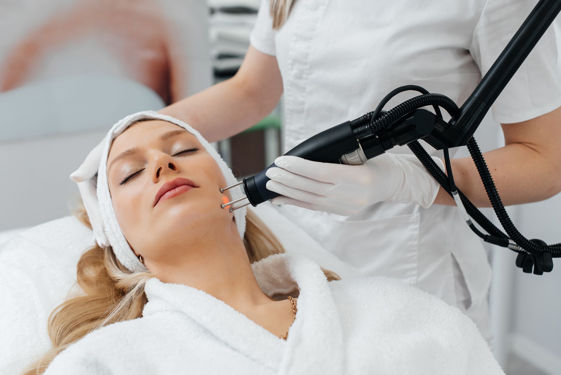 Woman receiving facial laser treatment in a spa, therapist holding device.