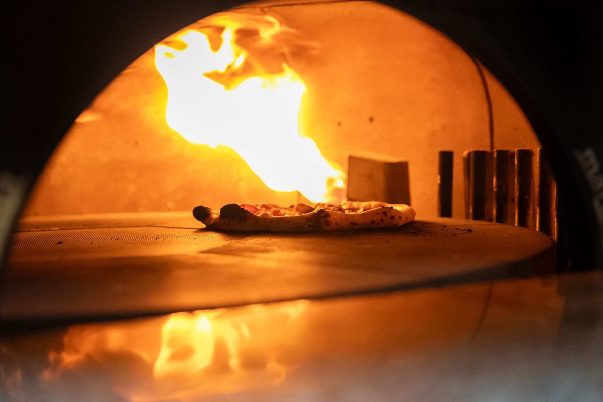 Pizza baking in a wood-fired oven with flames visible — Pizza in Huskisson, NSW
