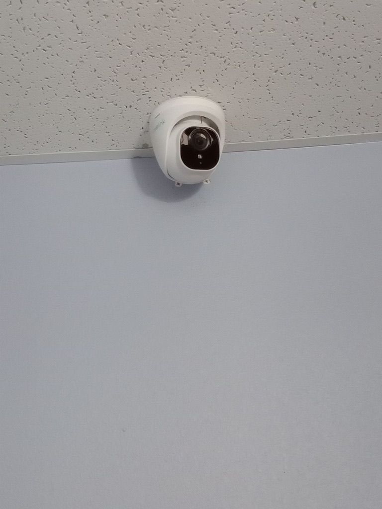 A security camera is hanging from the ceiling on a white wall.