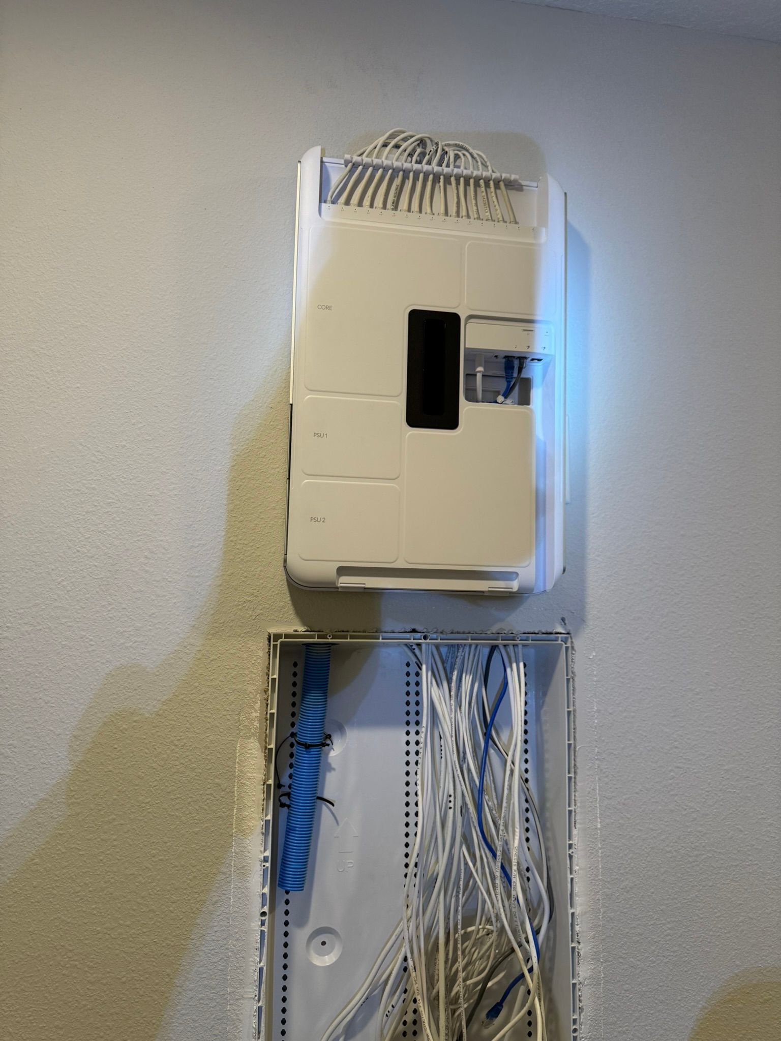 A white box with wires coming out of it is hanging on a wall.