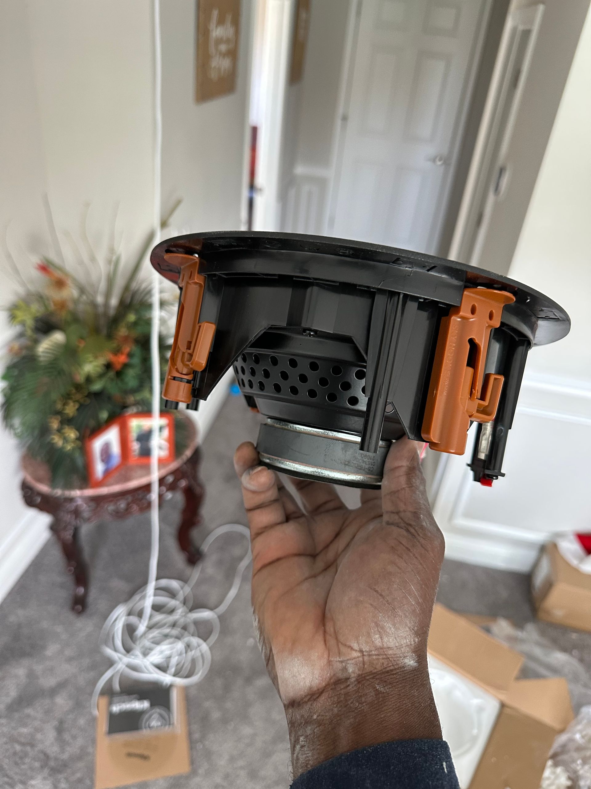 A person is holding a speaker in their hand in a living room.