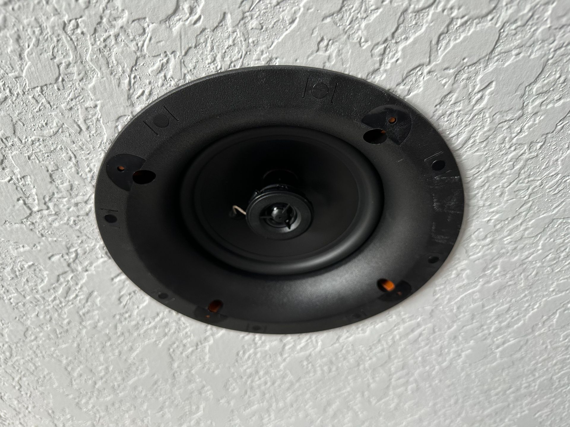 A black speaker is sitting on a white wall.