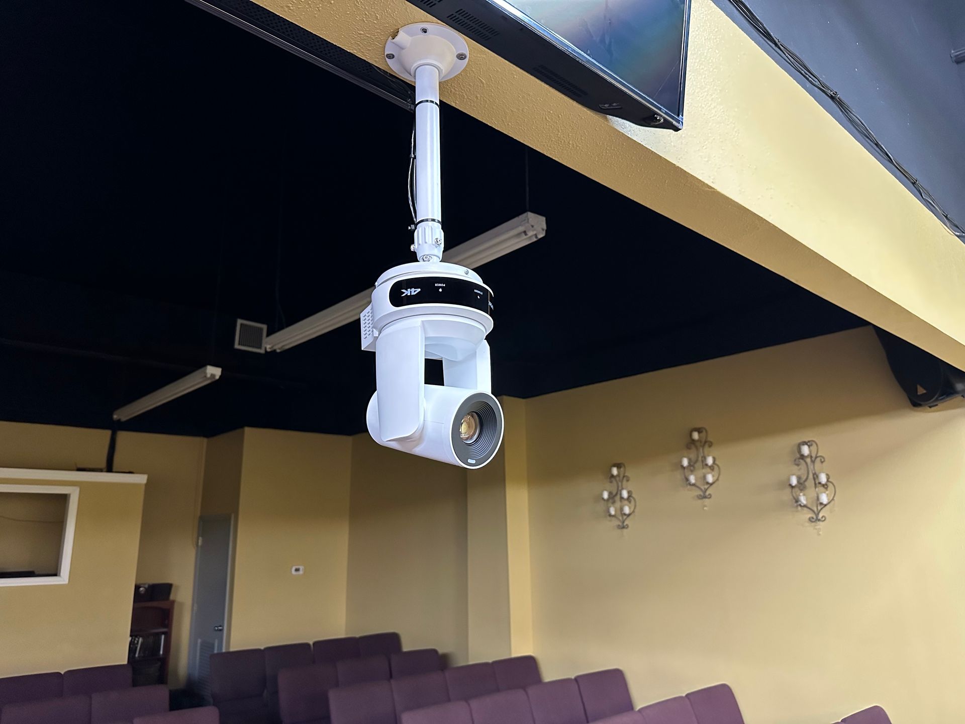 A projector is hanging from the ceiling in a room with purple chairs