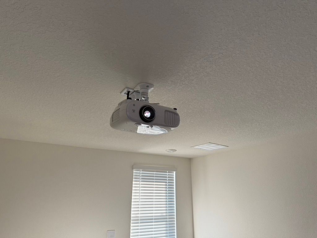 A projector is hanging from the ceiling in a room next to a window.