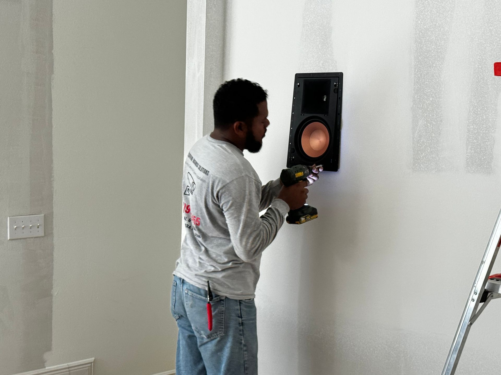 A man is using a drill to install a speaker on a wall.