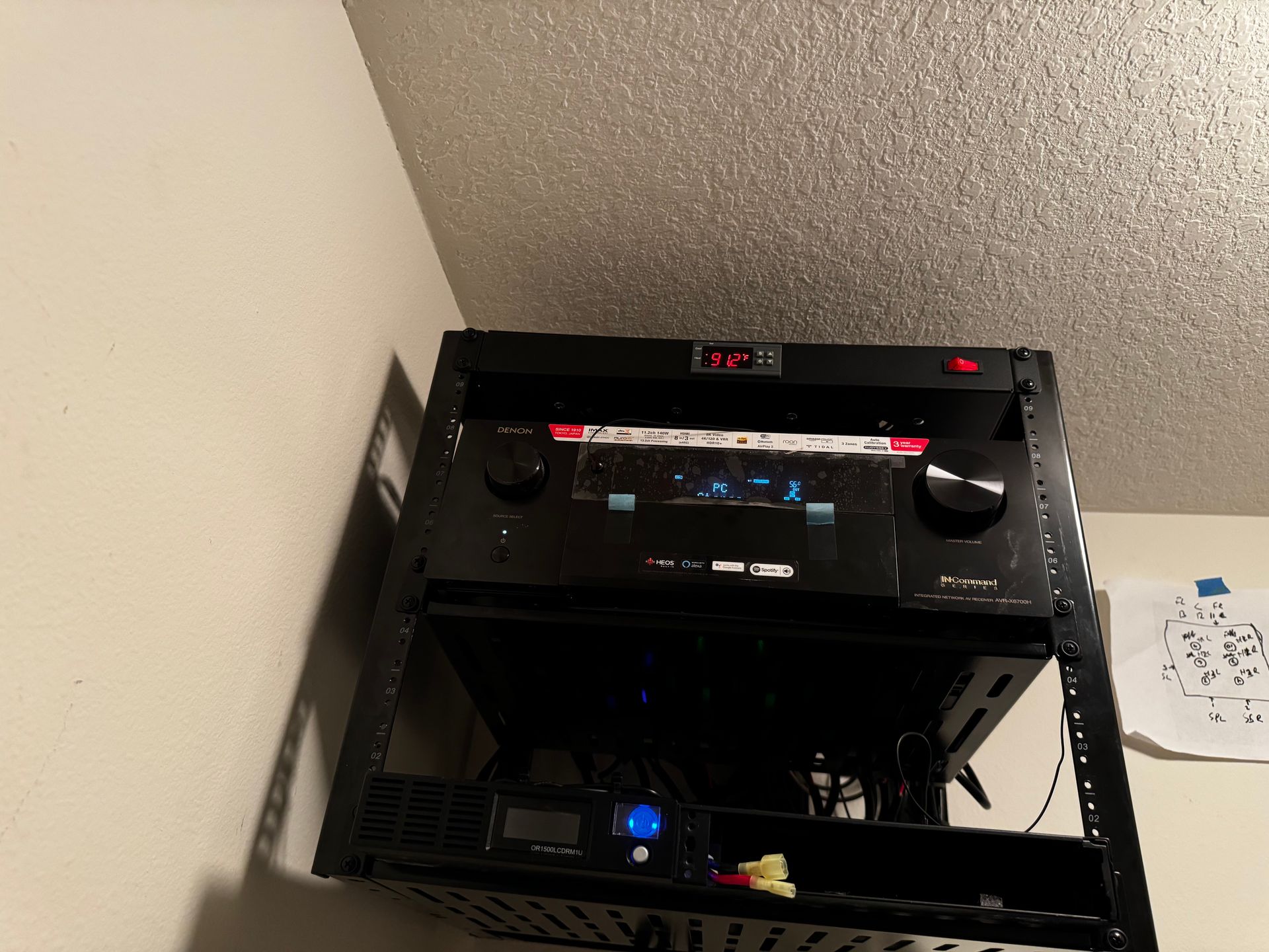 A black amplifier is mounted on a rack on a wall.