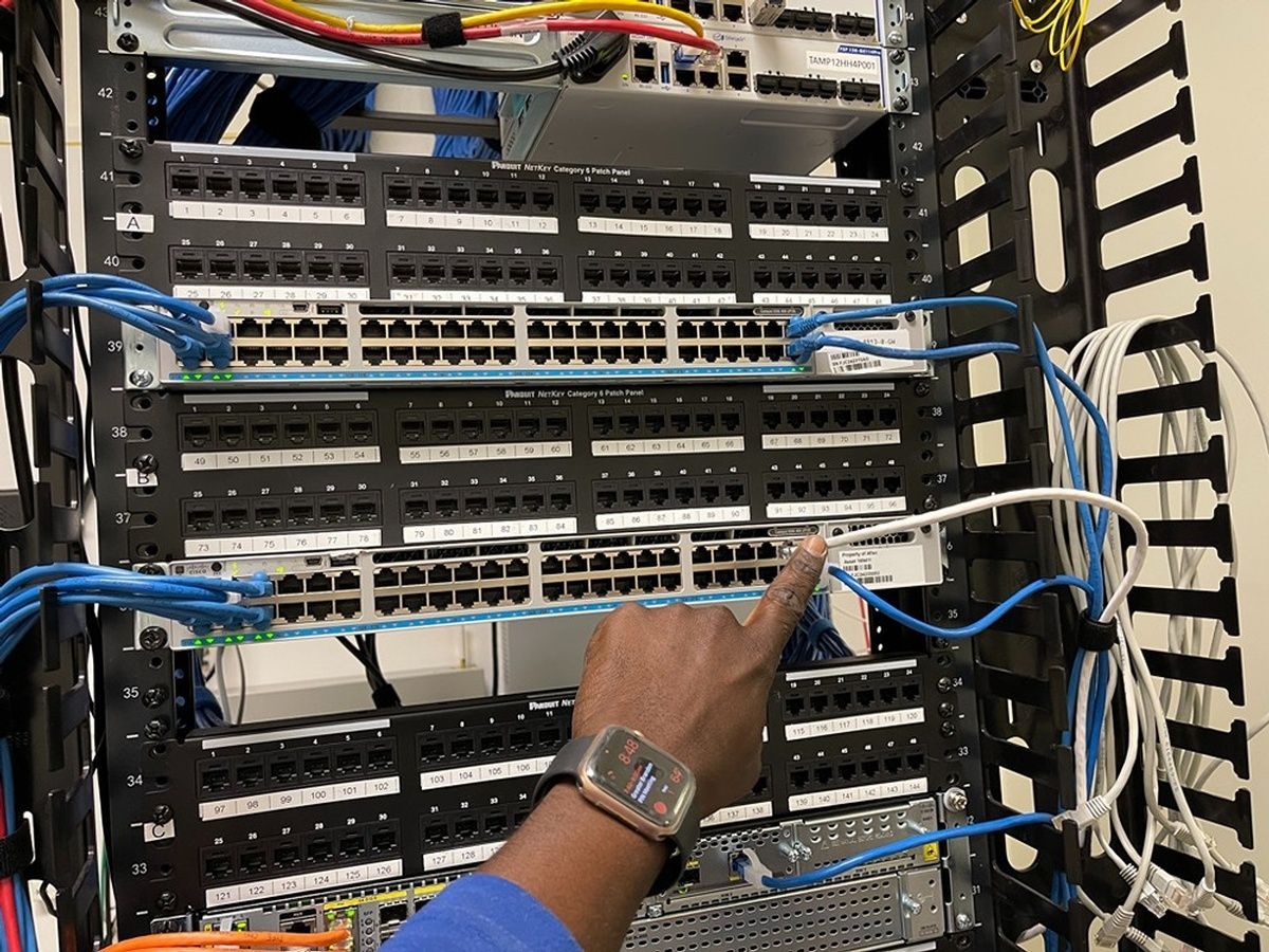 A person is pointing at a bunch of wires in a server rack.