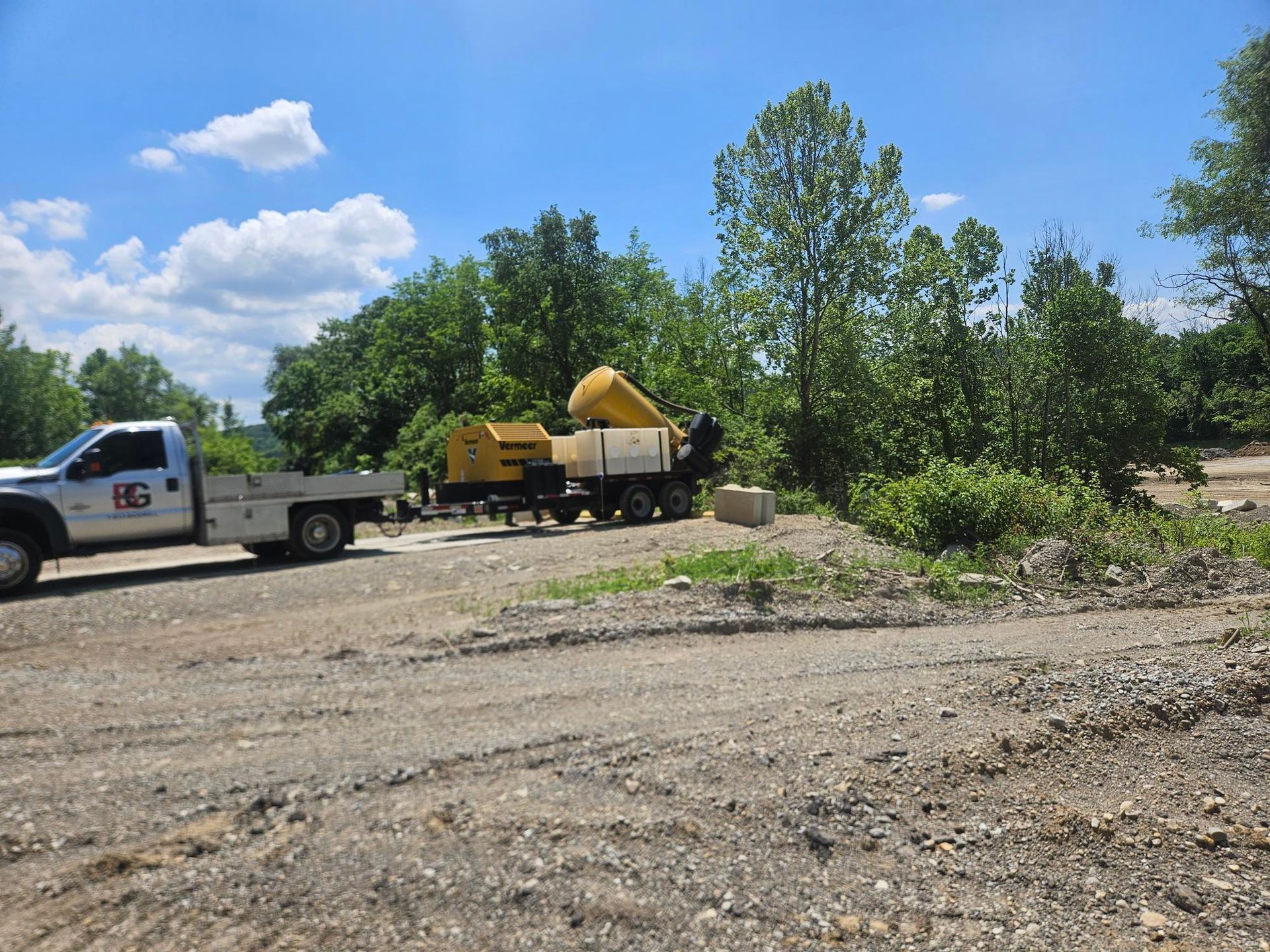 A white truck is driving down a dirt road with trees in the background.