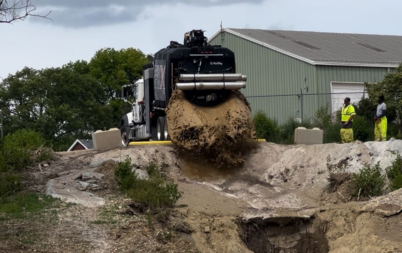 A truck is driving down a dirt road next to a building.