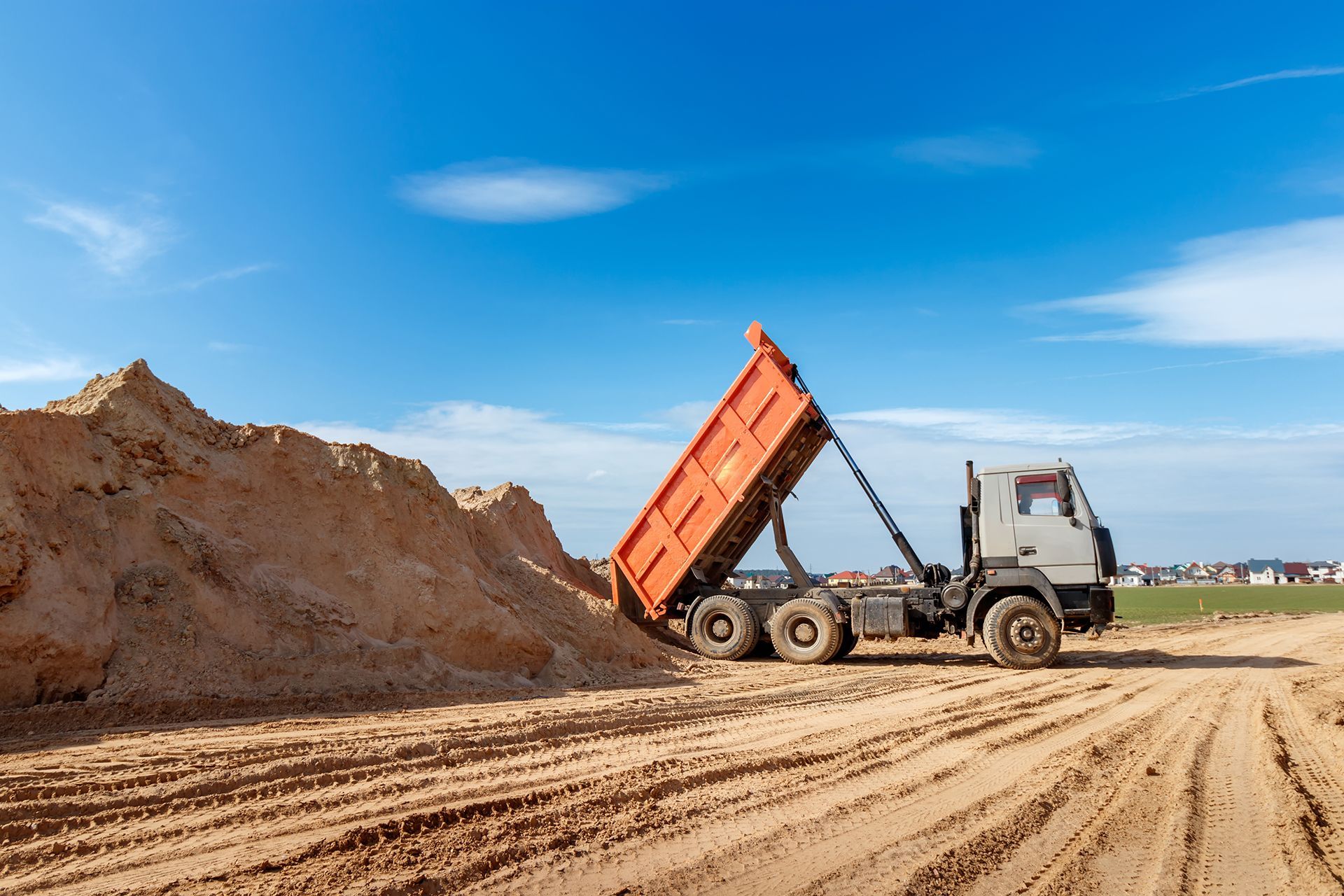 A dump truck is dumping sand on a dirt road.