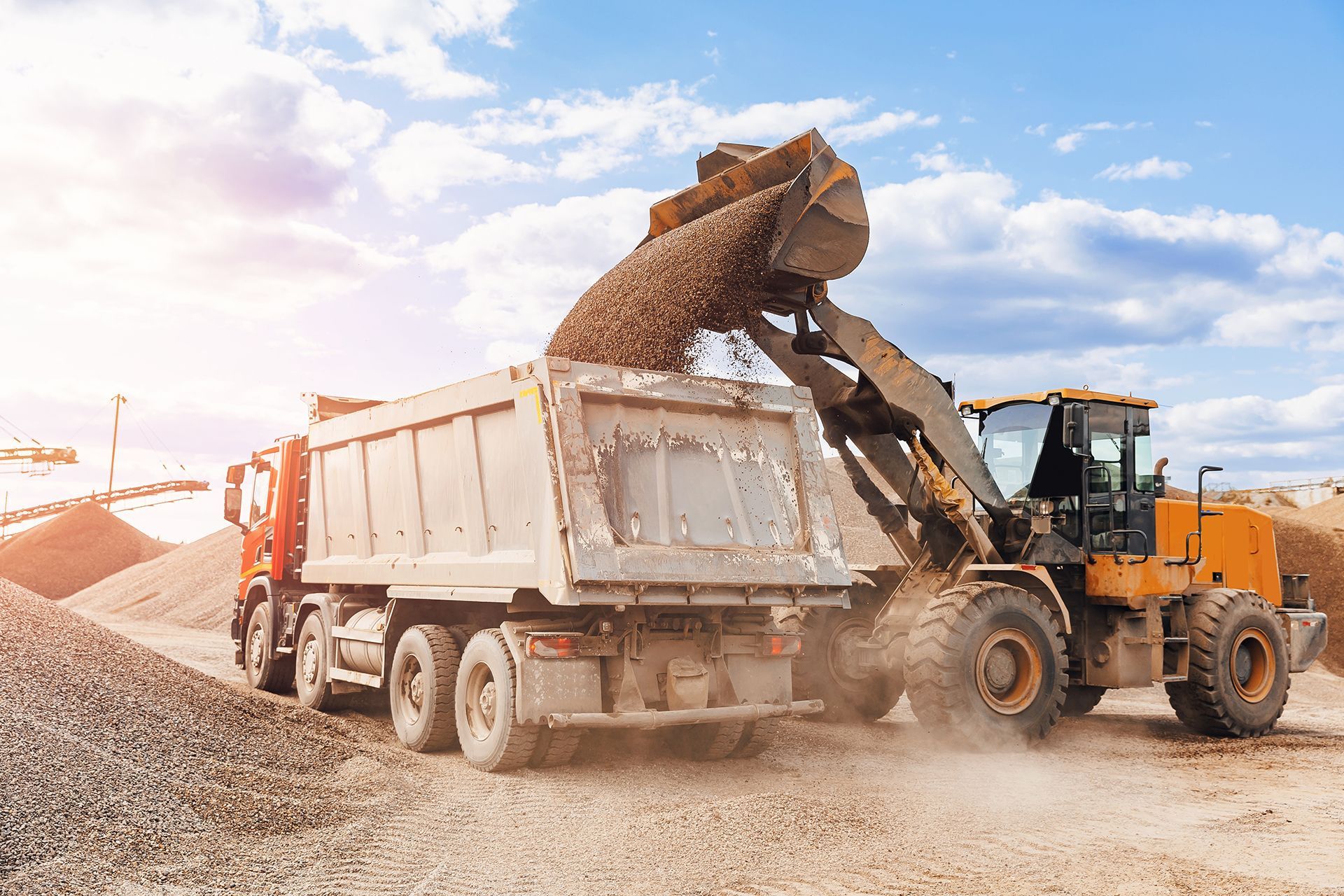 A dump truck is dumping sand into a pile.