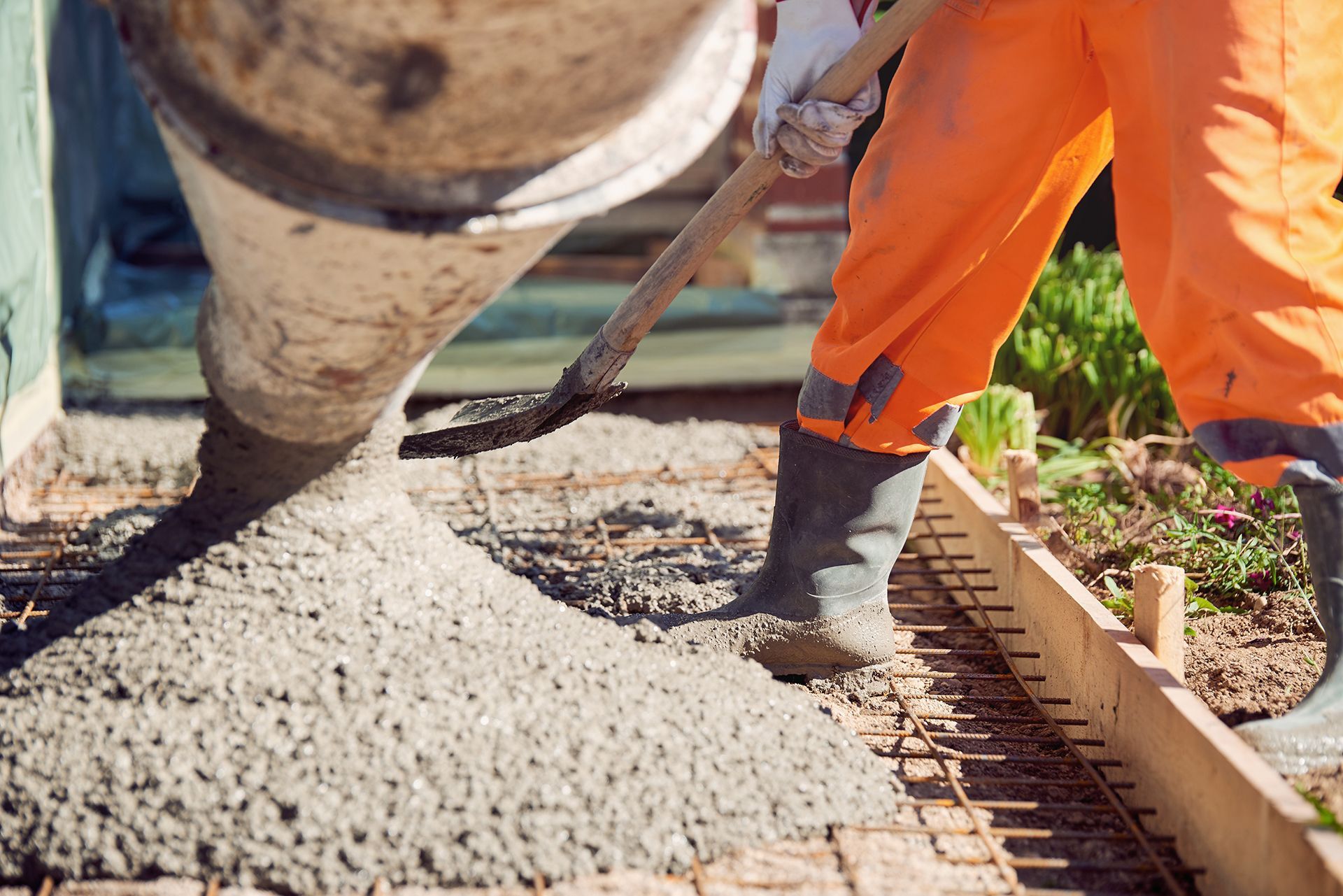 A man is pouring concrete on a sidewalk with a shovel.