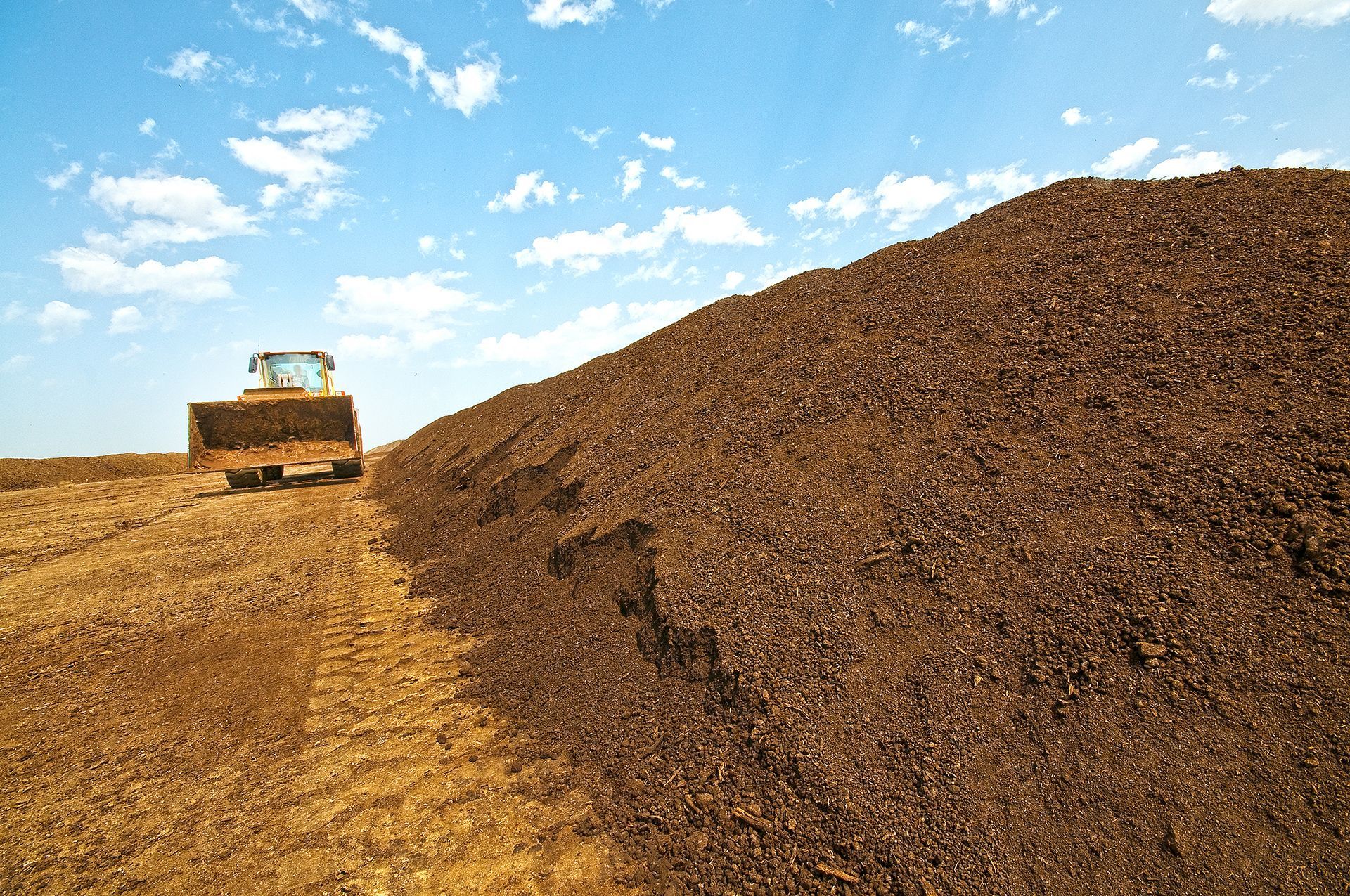 A bulldozer is driving down a dirt road next to a large pile of dirt.