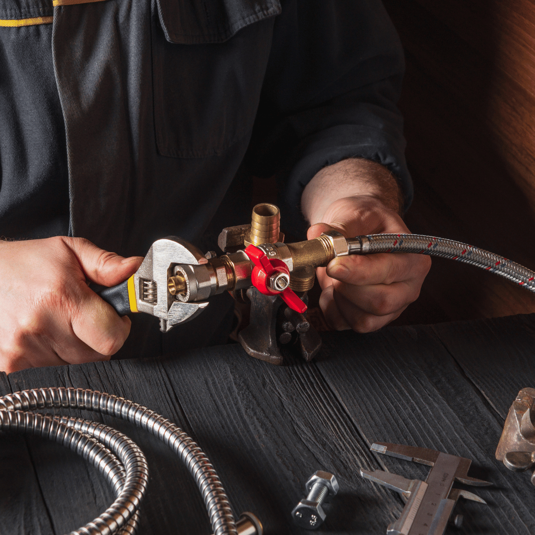 Plumber using a wrench to connect pipes, with tools on a wooden surface.
