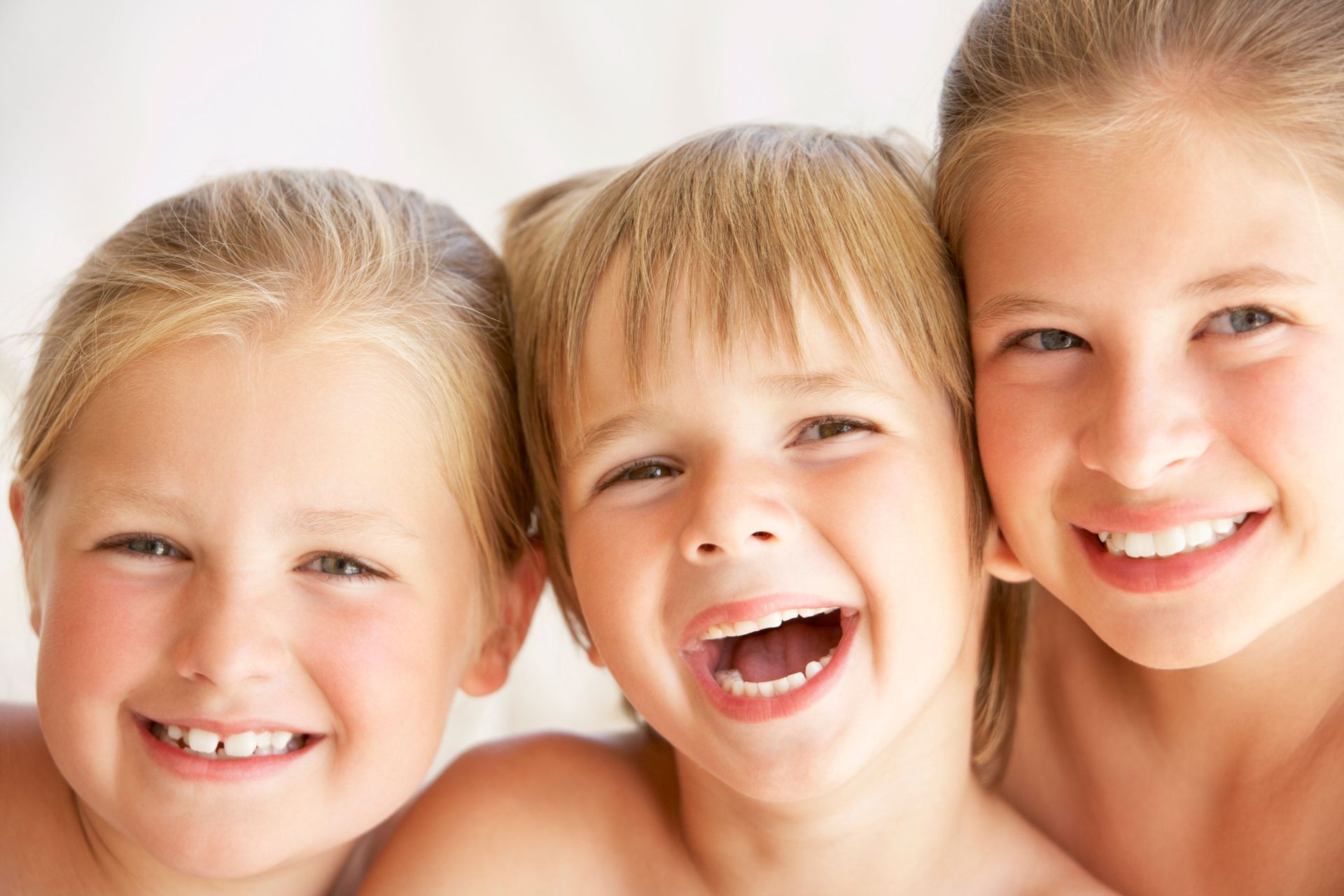 Three children , a boy and two girls , are smiling for the camera.