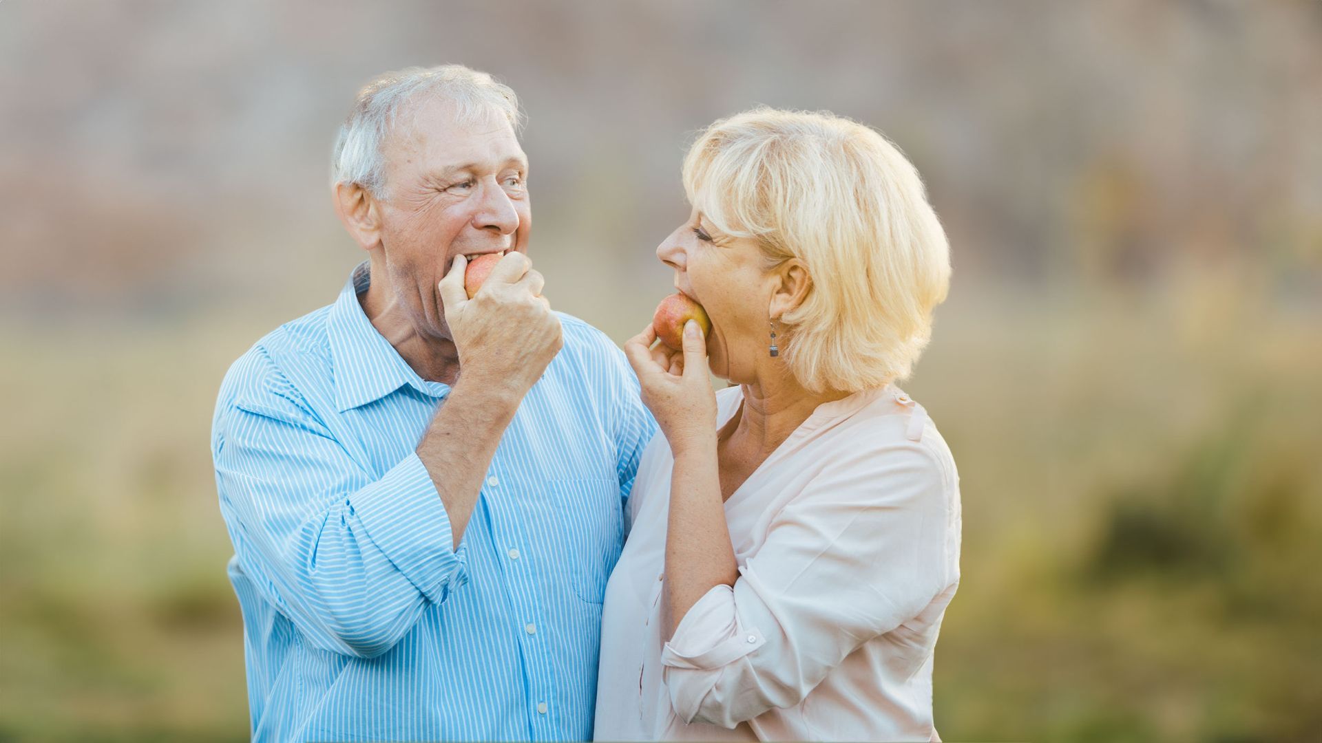 an elderly couple is eating an apple together .