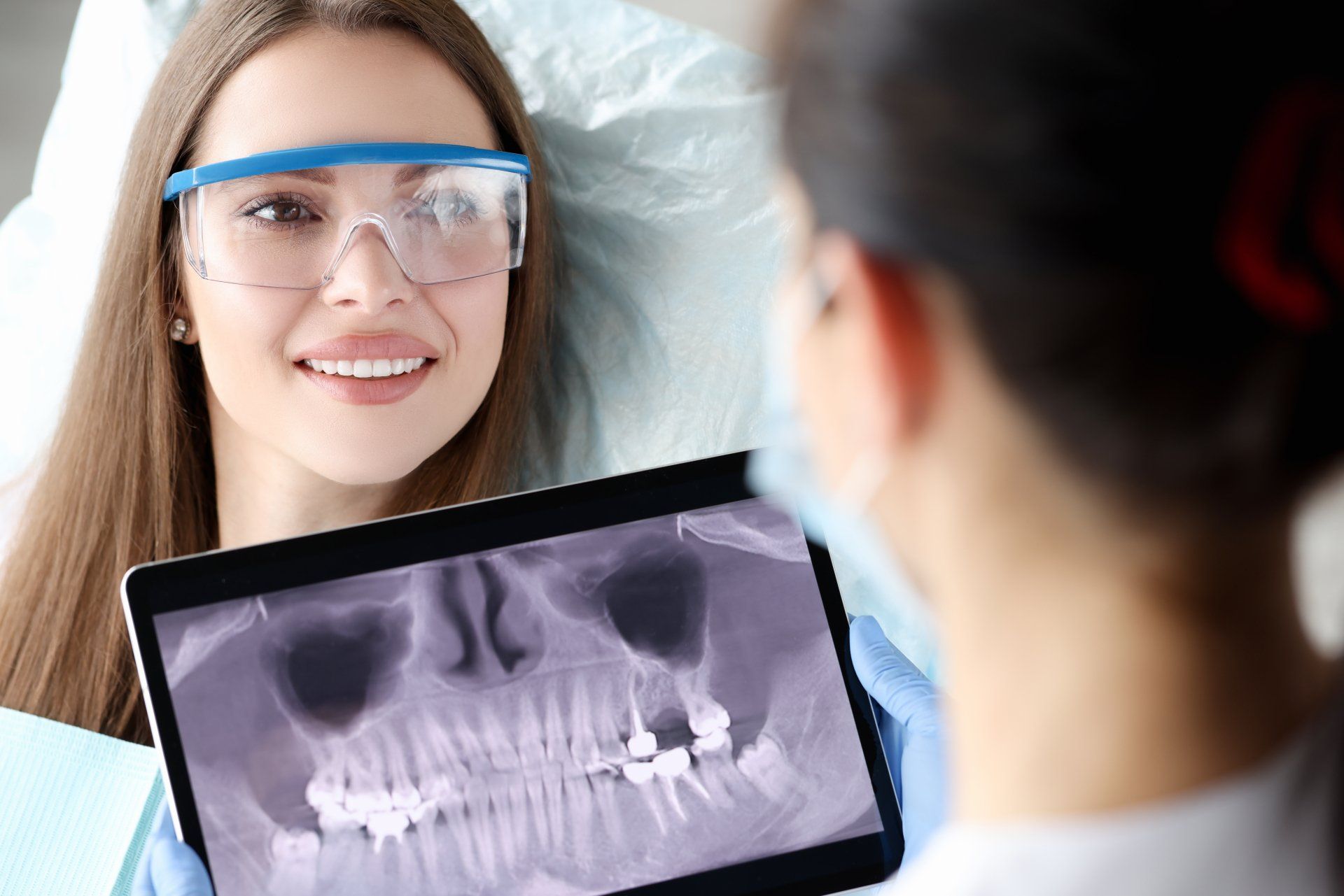 Una donna è seduta sulla poltrona del dentista e guarda una radiografia dei suoi denti.