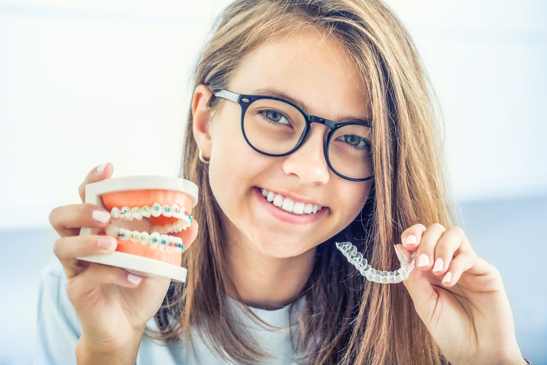 una ragazza con gli occhiali tiene in mano un modello di denti e un dispositivo invisibile