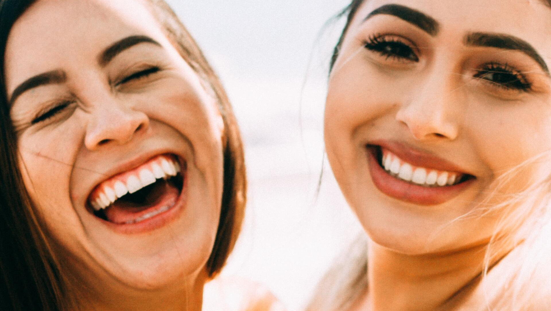 Due donne ridono insieme con gli occhi chiusi.